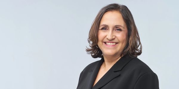 Smiling woman in a black blazer against a light background.