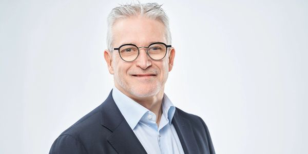 Smiling mature man in glasses wearing a suit and light blue shirt.