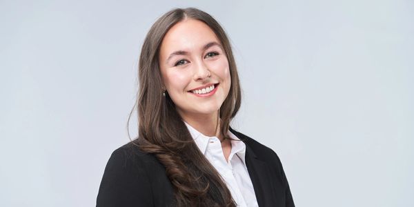 Smiling young woman in business attire posing against a plain background.