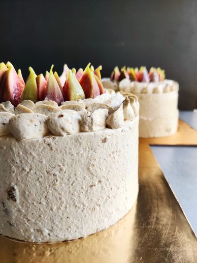 Two elegant cakes with fig-topped creamy frosting on a gold surface.