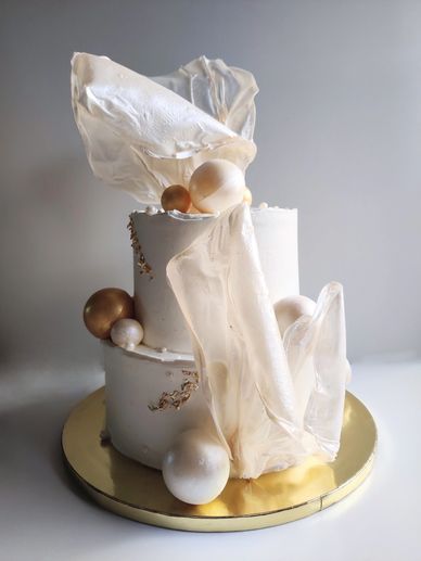 Elegant two-tier cake with gold and white spheres and delicate translucent decorations.