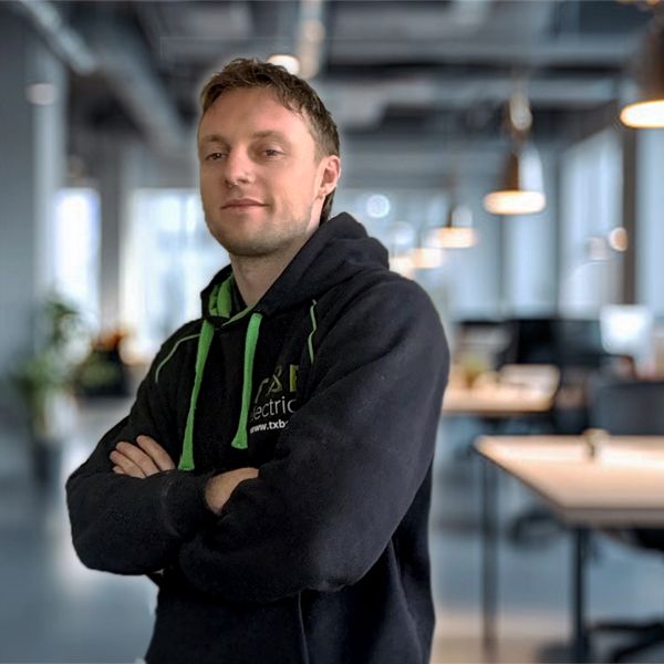 Confident man in black hoodie with green accents stands in a modern office.