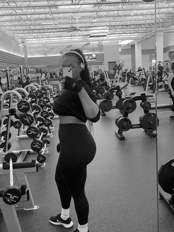 Woman in black workout clothes posing for a gym mirror selfie.