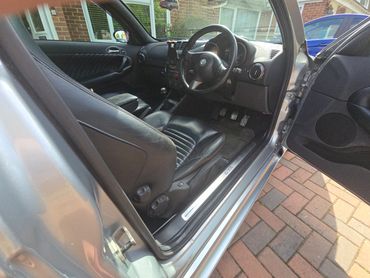 Interior of a silver Alfa Romeo GTA with black leather seats and manual transmission.