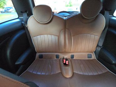 Brown leather backseat of a car with headrests and seatbelt buckles.