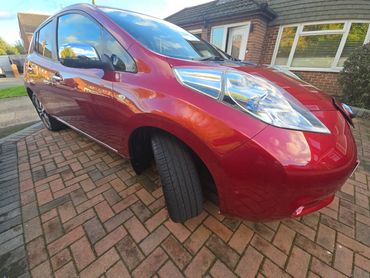 A shiny red car parked on a brick driveway in front of a house.