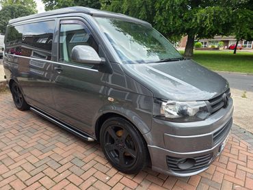 Sleek gray Volkswagen van parked on a brick driveway.