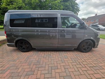 Sleek gray van with black rims parked on a brick driveway.