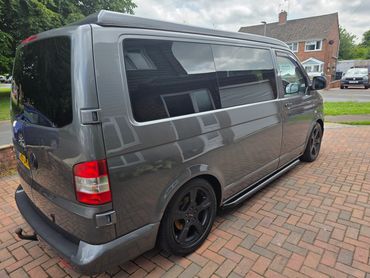 Gray van with black wheels parked on a brick driveway.