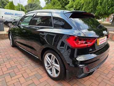 Sleek black Audi A1 parked on a brick driveway with reflective windows and modern taillights.
