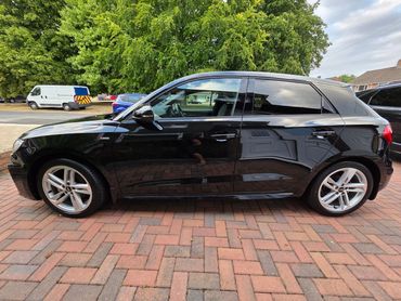 Shiny black Audi parked on a brick driveway with green trees in the background.