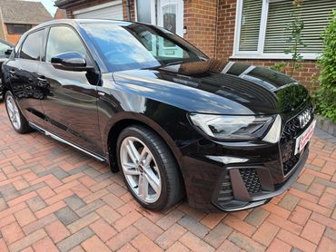 Glossy black Audi parked on a brick driveway next to a house.