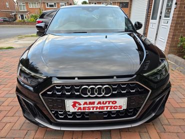 Front view of a shiny black Audi with AM Auto Aesthetics plate.