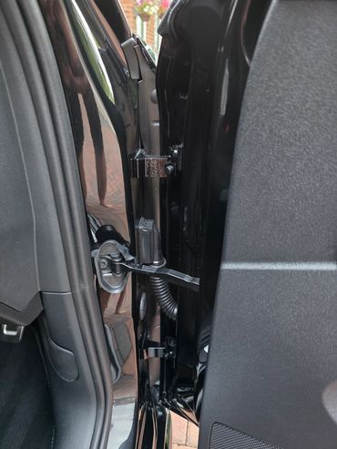 Close-up of a car door hinge and wiring area.