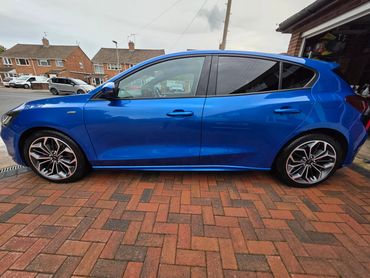 Sleek blue hatchback car parked on a brick driveway beside a garage.