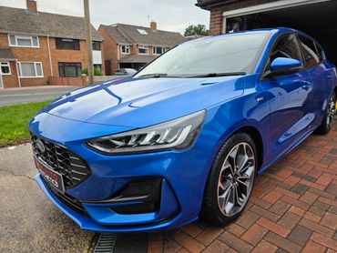 A shiny blue Ford car parked on a driveway in a residential area.