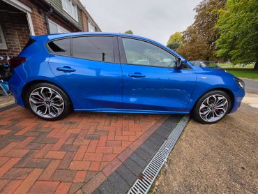 A sleek blue hatchback car parked on a driveway beside a house.