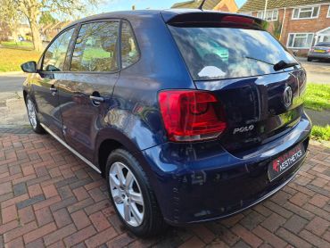A shiny blue Volkswagen Polo parked on a brick driveway on a sunny day.