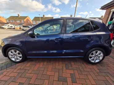 Side view of a dark blue Volkswagen hatchback parked on a brick driveway.