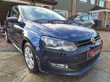 Blue Volkswagen parked outside a house with minor scratches on the front wheel arch.