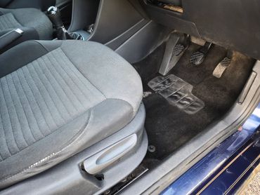 Inside view of a car's driver's seat with gear stick and pedals.