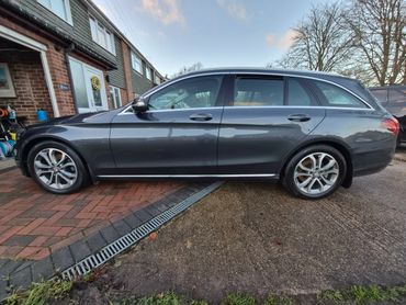 Gray station wagon parked halfway on driveway and pavement.