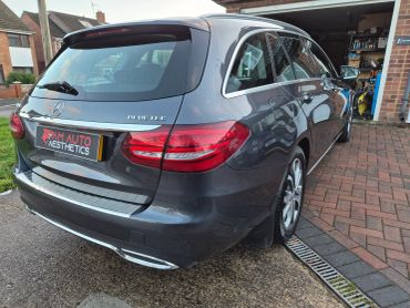Rear side view of a grey Mercedes Bluetec estate car parked by a driveway.