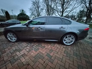 Dark grey luxury sedan parked on a brick driveway at dusk.