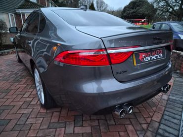 Rear side view of a sleek Jaguar XF parked on a brick driveway.