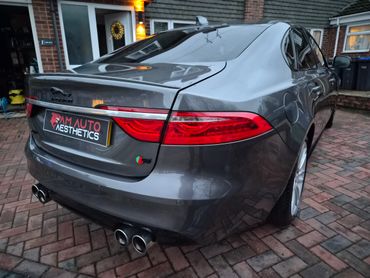 Rear view of a sleek gray Jaguar S car parked on a brick driveway.