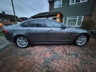 Sleek gray sedan parked on a brick driveway in front of a house at dusk.