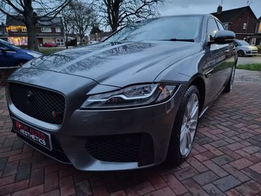Sleek grey Jaguar parked on a brick driveway at dusk.