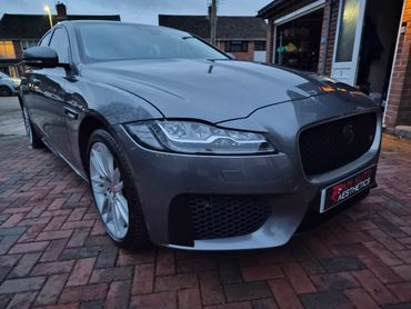 A sleek gray Jaguar parked on a brick driveway at dusk.