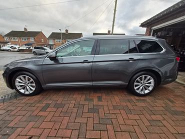 Side view of a sleek gray Volkswagen estate car parked on a brick driveway.