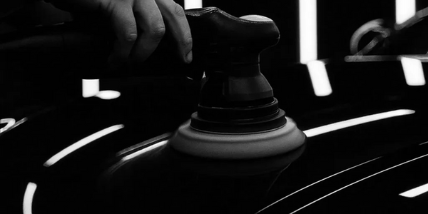 Detailing studio black and white image of DA polisher on bonnet of black shiny car