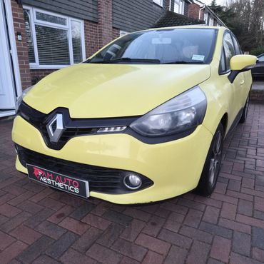 Yellow Renault car parked on driveway in front of a brick house.