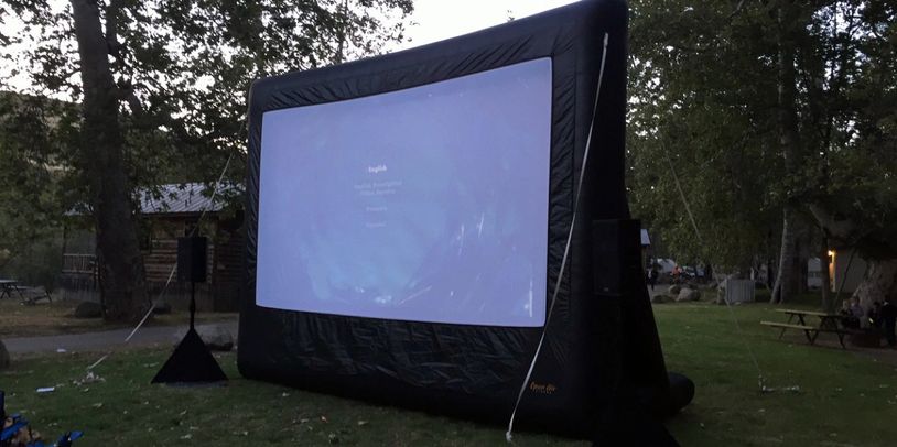 Outdoor inflatable movie screen set up in a park at dusk.