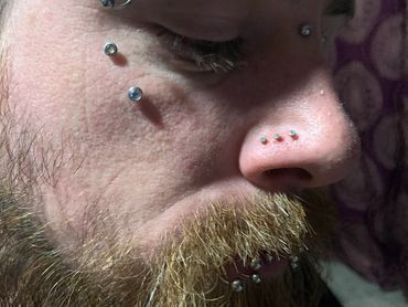 Close-up of a man’s face featuring multiple facial piercings, including symmetrical dermals & more
