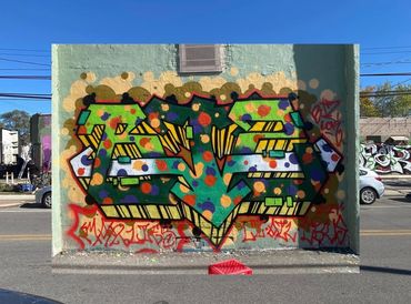 Colorful graffiti mural with bold lettering, polka dot overlay, & abstract 3D shapes on a city wall