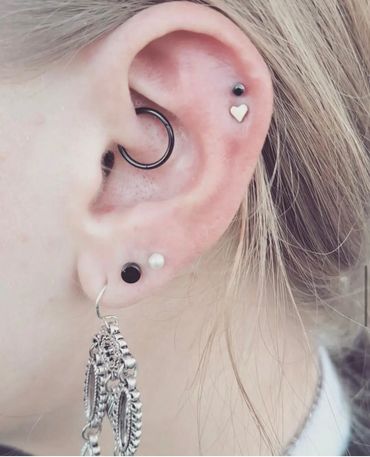 Curated ear piercings featuring a black conch hoop, helix stud with silver heart, lobe studs.