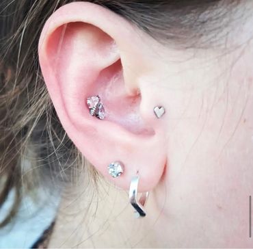 Curated ear piercings featuring a pink gemstone daith cluster, silver heart helix stud.