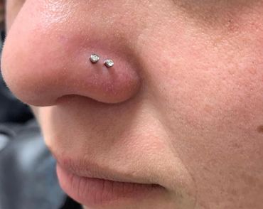 Close-up of a fresh double nostril piercing with two silver studs placed side by side on the left.