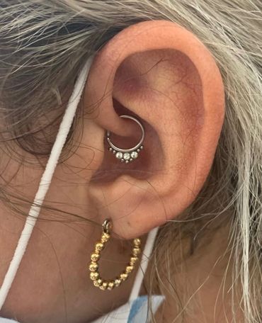 Close-up of an ear with a daith piercing featuring a silver hoop adorned with clear gemstones.