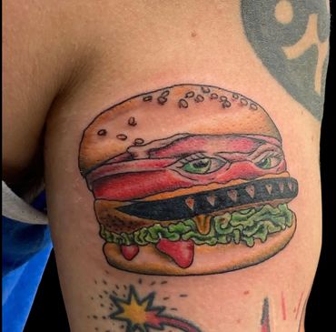 Tattoo of a fierce cheeseburger with sharp teeth and eyes— at Stoic Body Art in Columbus, Ohio.