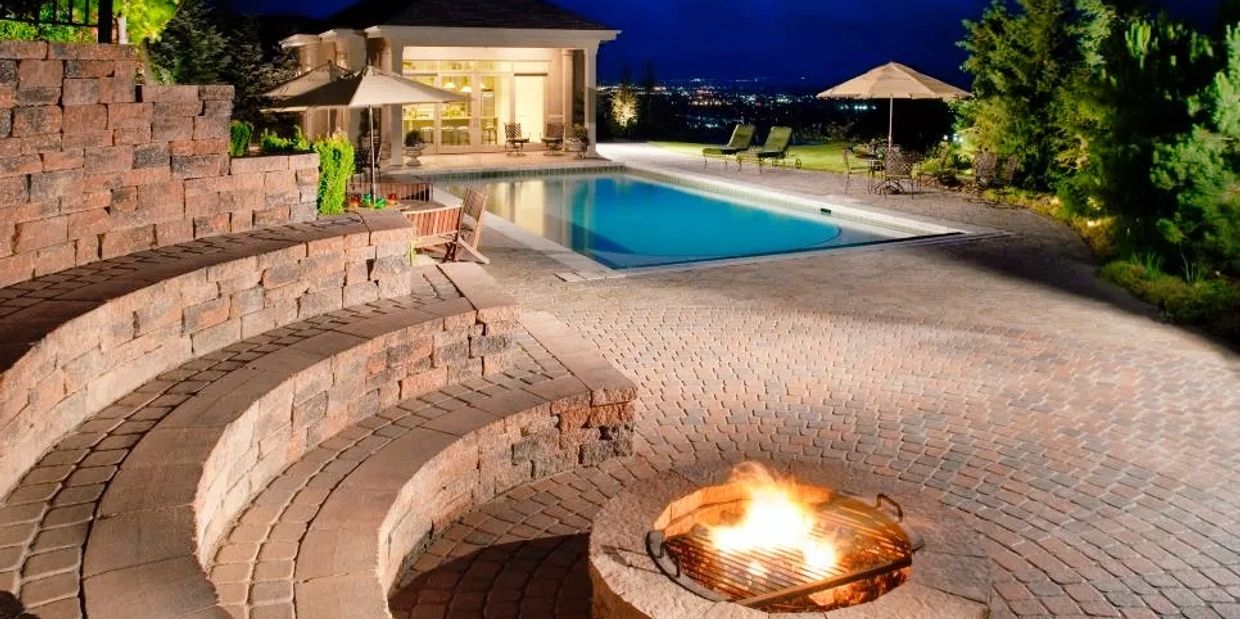 Elegant outdoor patio with fire pit, pool, and seating area at night.
