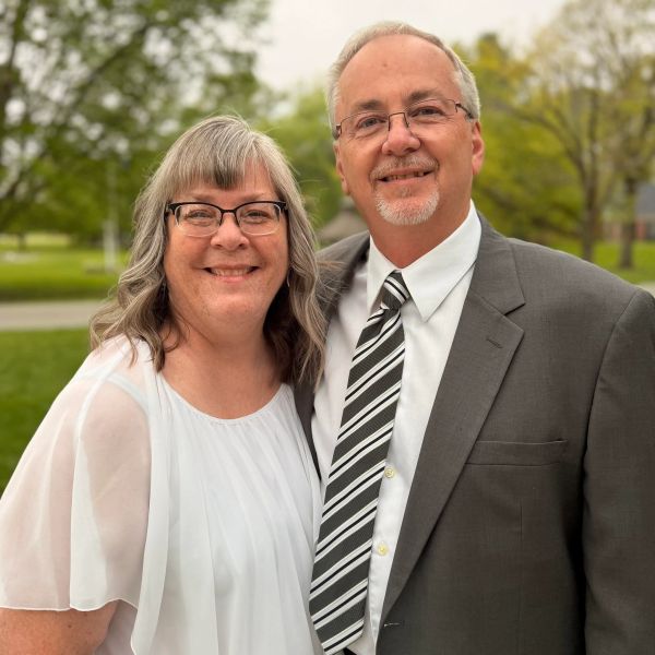 Smiling couple posing outdoors, dressed formally.
