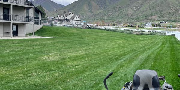 A large green lawn with a red lawn mower and mountains in the background.