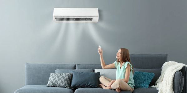 Woman controlling air conditioner with remote on sofa.