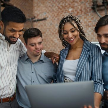 Diverse group happily collaborating over a laptop in a casual workspace.