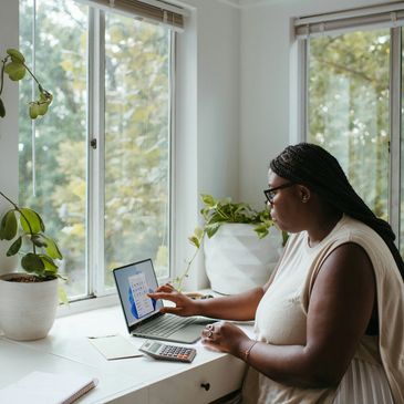 Woman working on data analysis on laptop by a window.